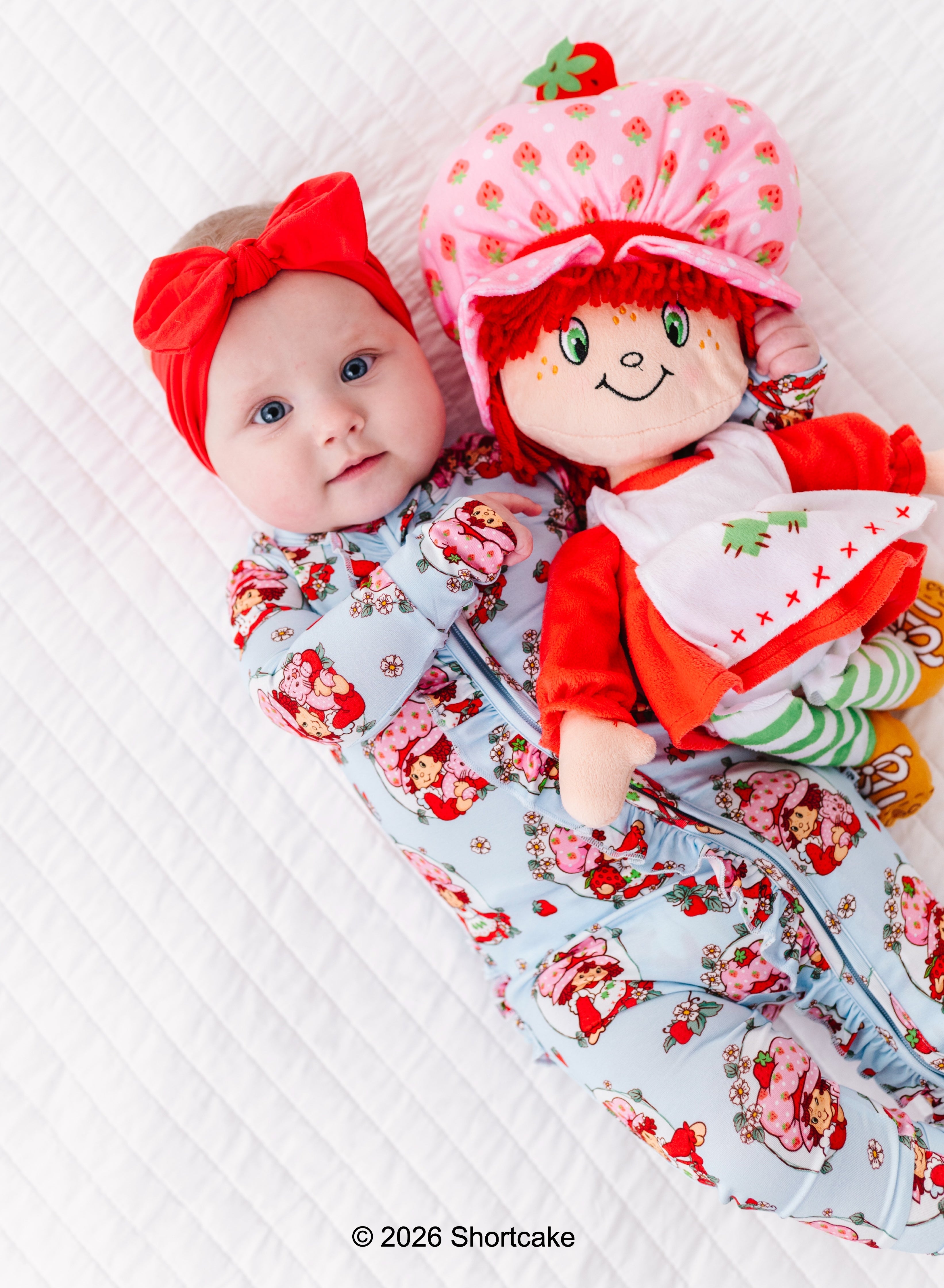 Baby in a Strawberry Shortcake™ bamboo convertible romper, cuddling with a Strawberry Shortcake™ doll
